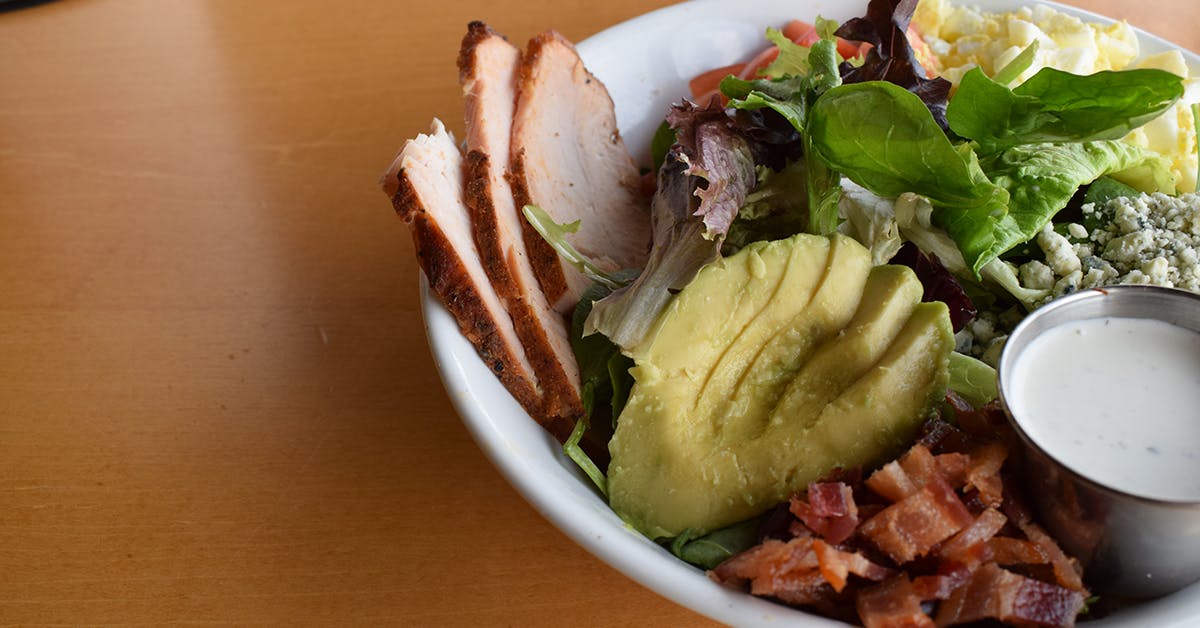 a white bowl filled with chopped avocado, salad and grilled chicken