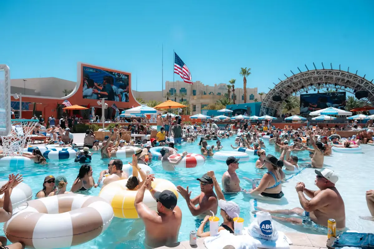 Crowded pool with floats, flag flying, peak-day energy at Tailgate Beach Club