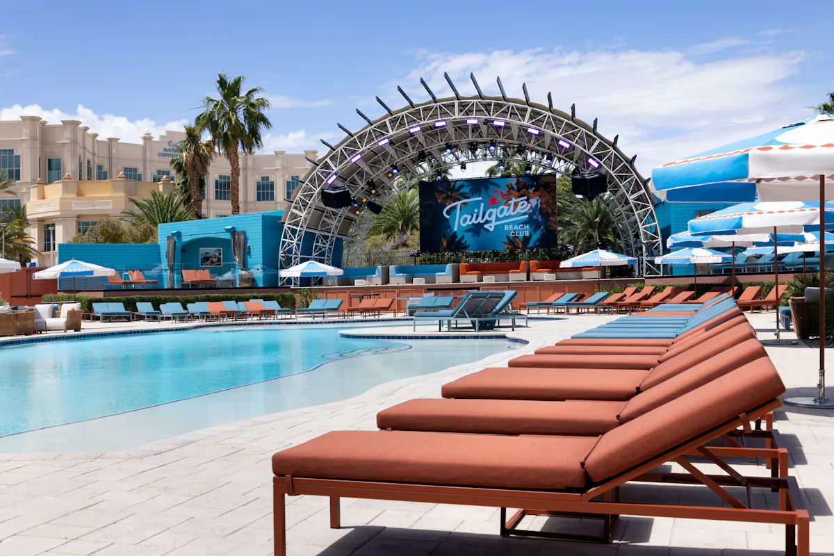 Coral loungers lining pool with stage arch behind at Tailgate Beach Club