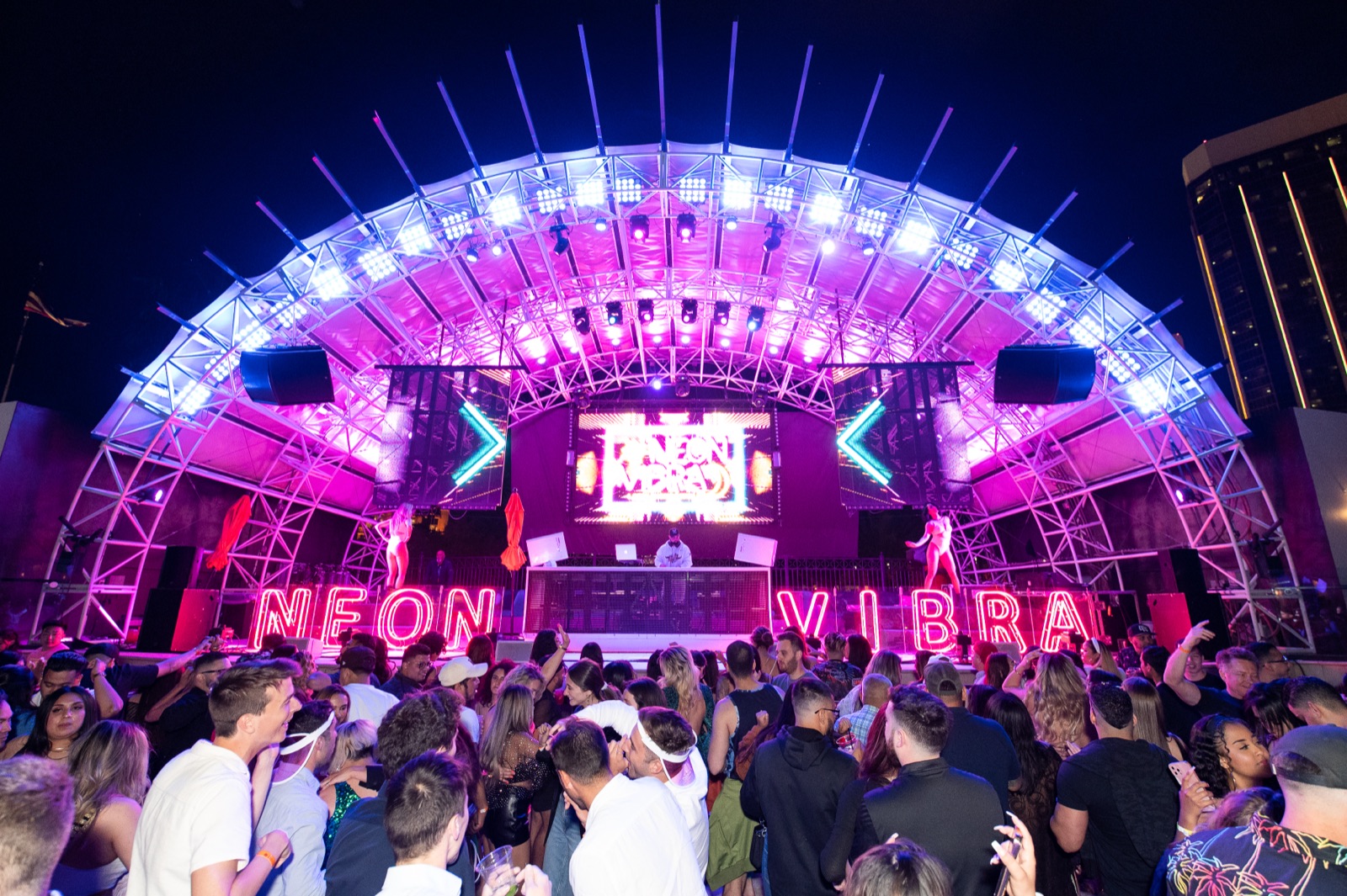 Neon-letter stage with DJ and dancers at Neon Vibra