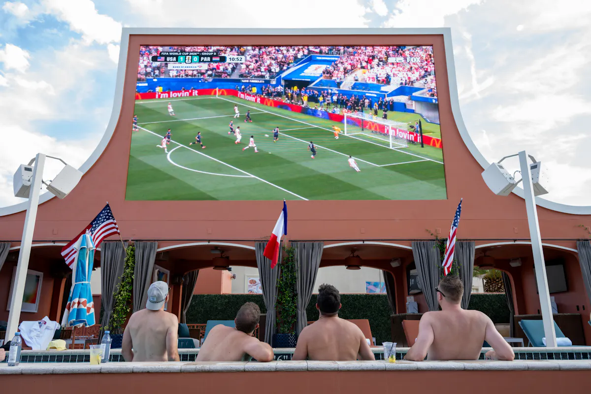 Swimmers watching World Cup match on giant screen with flags at Tailgate Beach Club