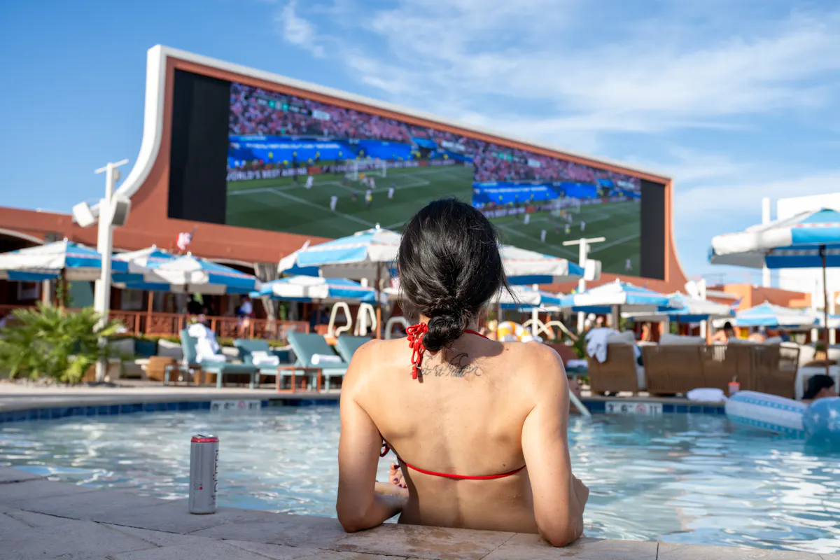 Woman in pool from behind watching match on big screen at Tailgate Beach Club