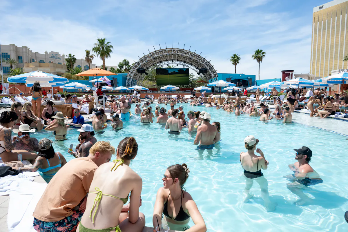 Crowded pool with stage arch and palms at Tailgate Beach Club