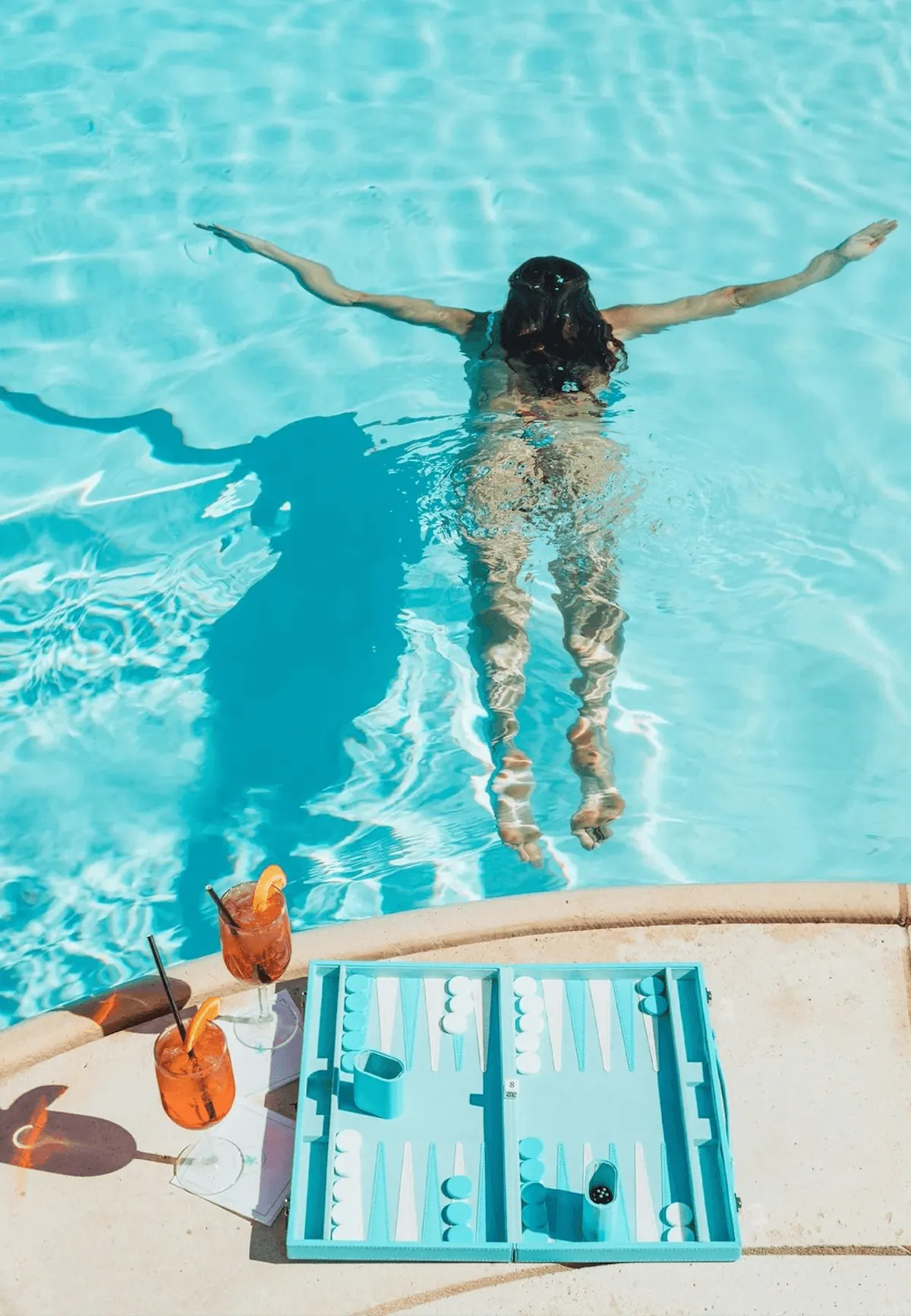 Overhead of woman swimming past poolside backgammon board at Tailgate Beach Club
