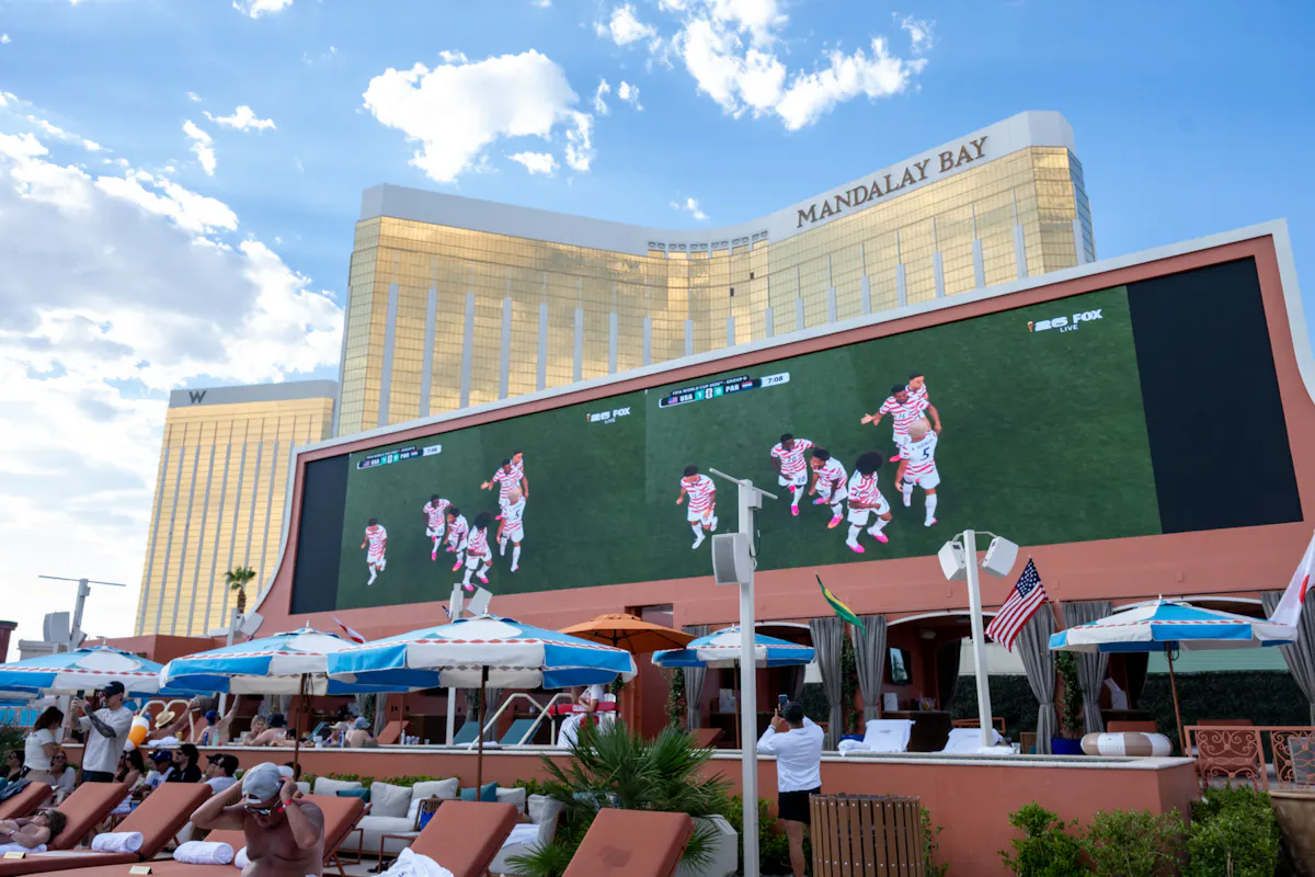 Players celebrating on giant screen above full pool deck at Tailgate Beach Club
