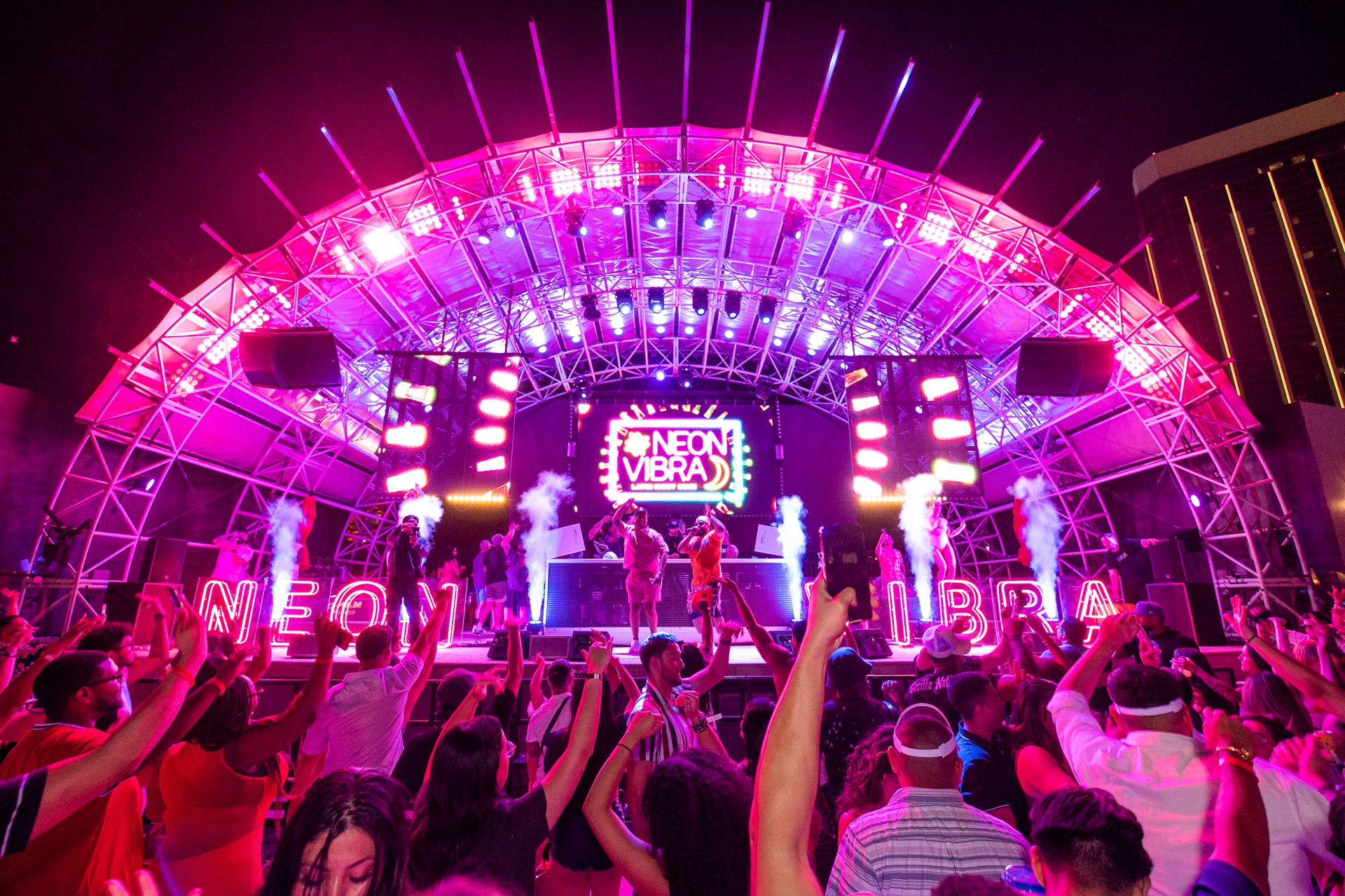 Neon Vibra Latin night at Tailgate Beach Club: pink-lit stage with giant neon letters and CO2 cannons over the crowd