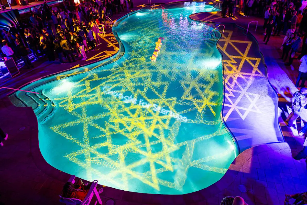 Aerial view of the main pool with a glowing light pattern projected across the water at night