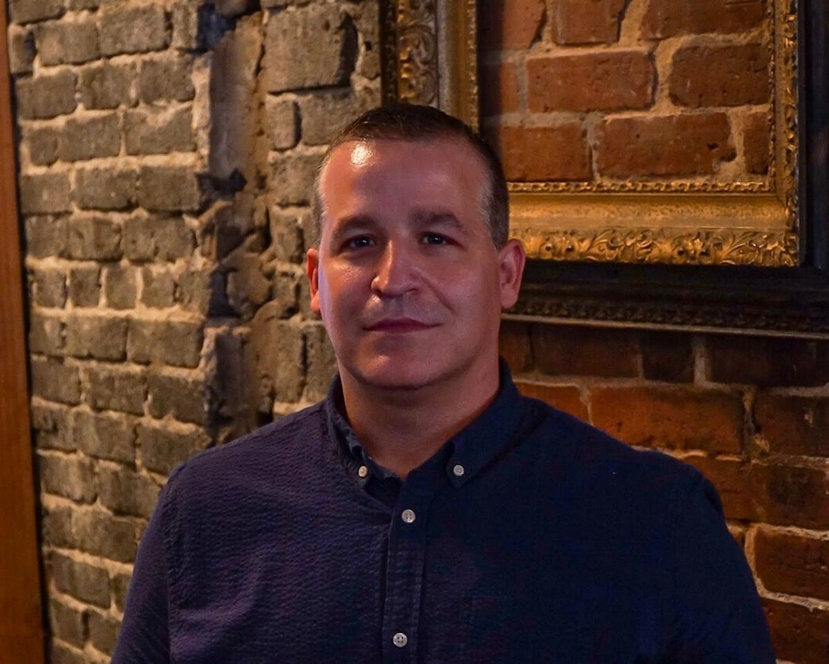 mark standish standing in front of a brick wall posing for the camera