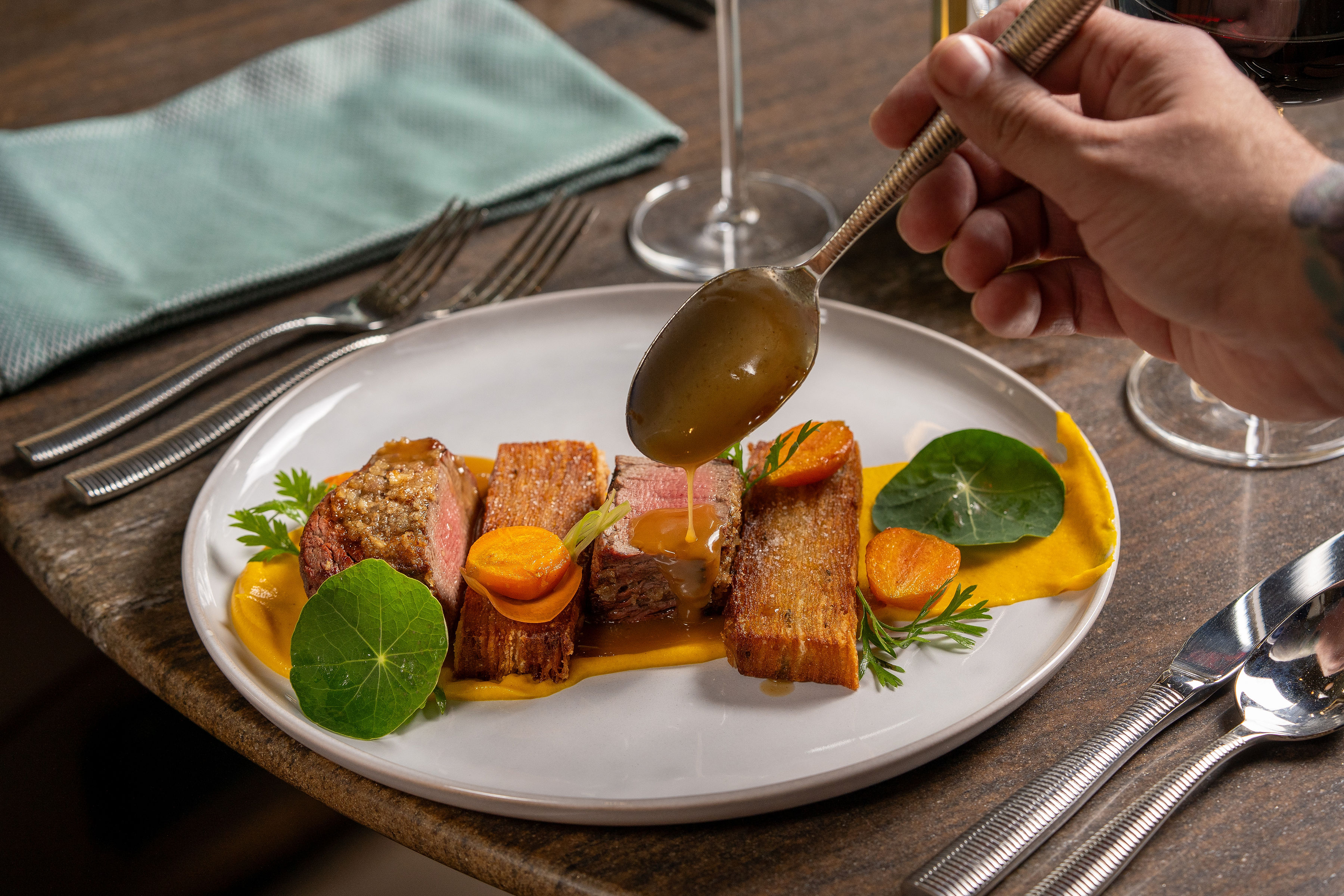 a person pouring sauce on a plate of meat