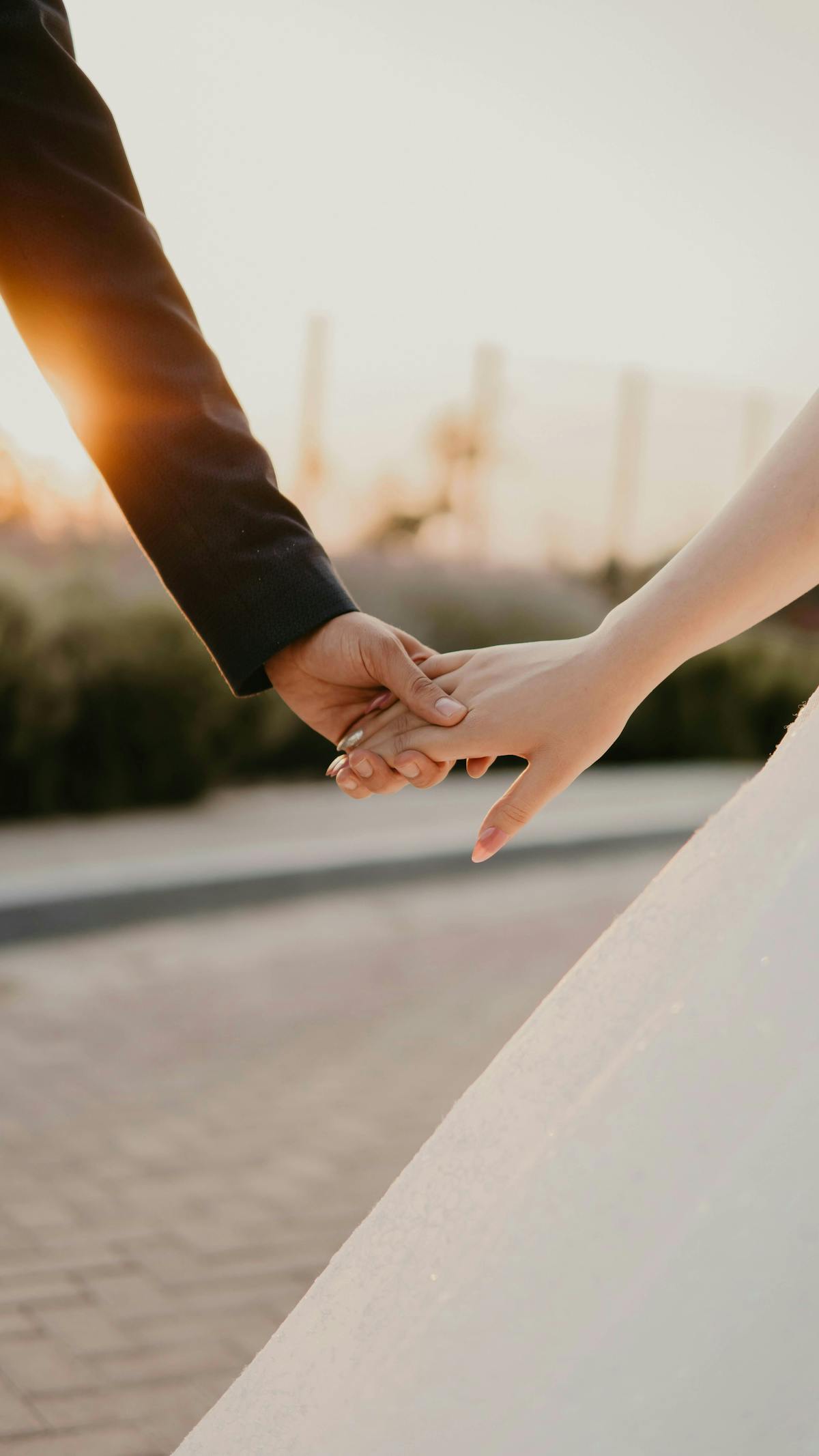 A newlywed couple holding hands at sunset, symbolizing love and commitment, with a blurred outdoor background somewhere in Vancouver