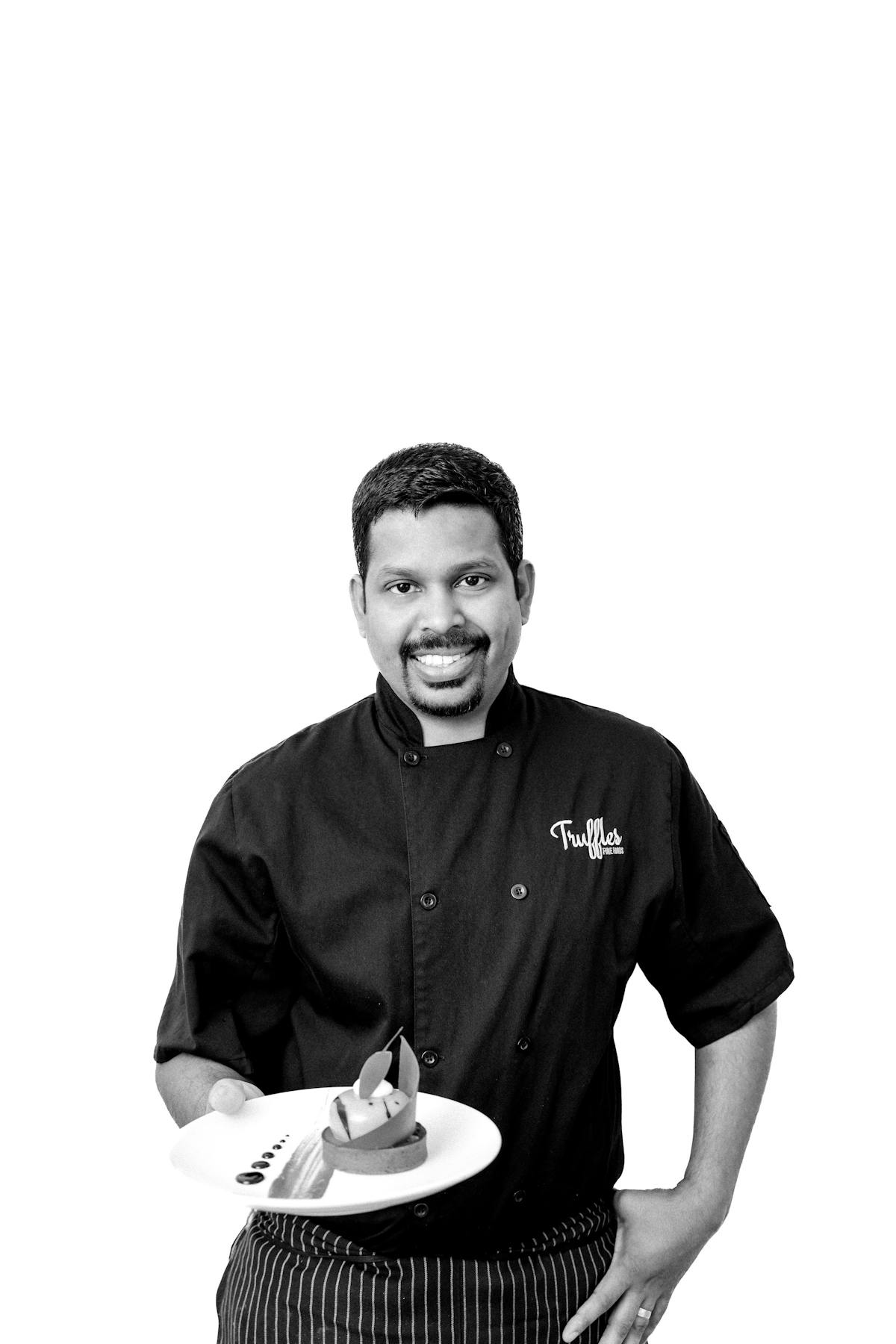 Black and white portrait of Pastry Chef Benny Daniel, holding a plate of desserts