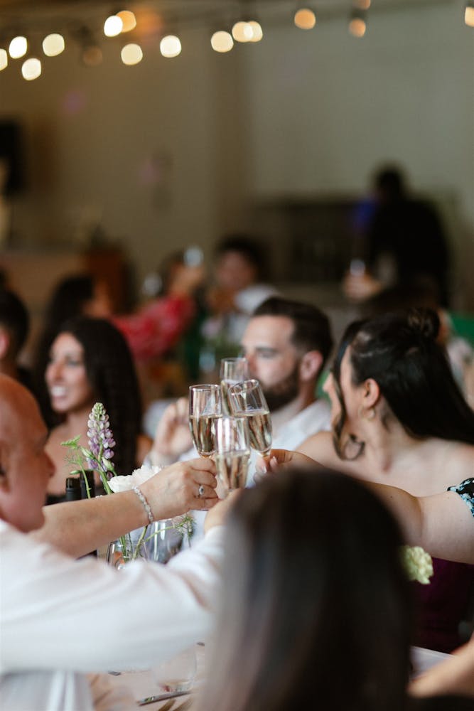 people at a wedding cheering and clicking wine glasses over a table