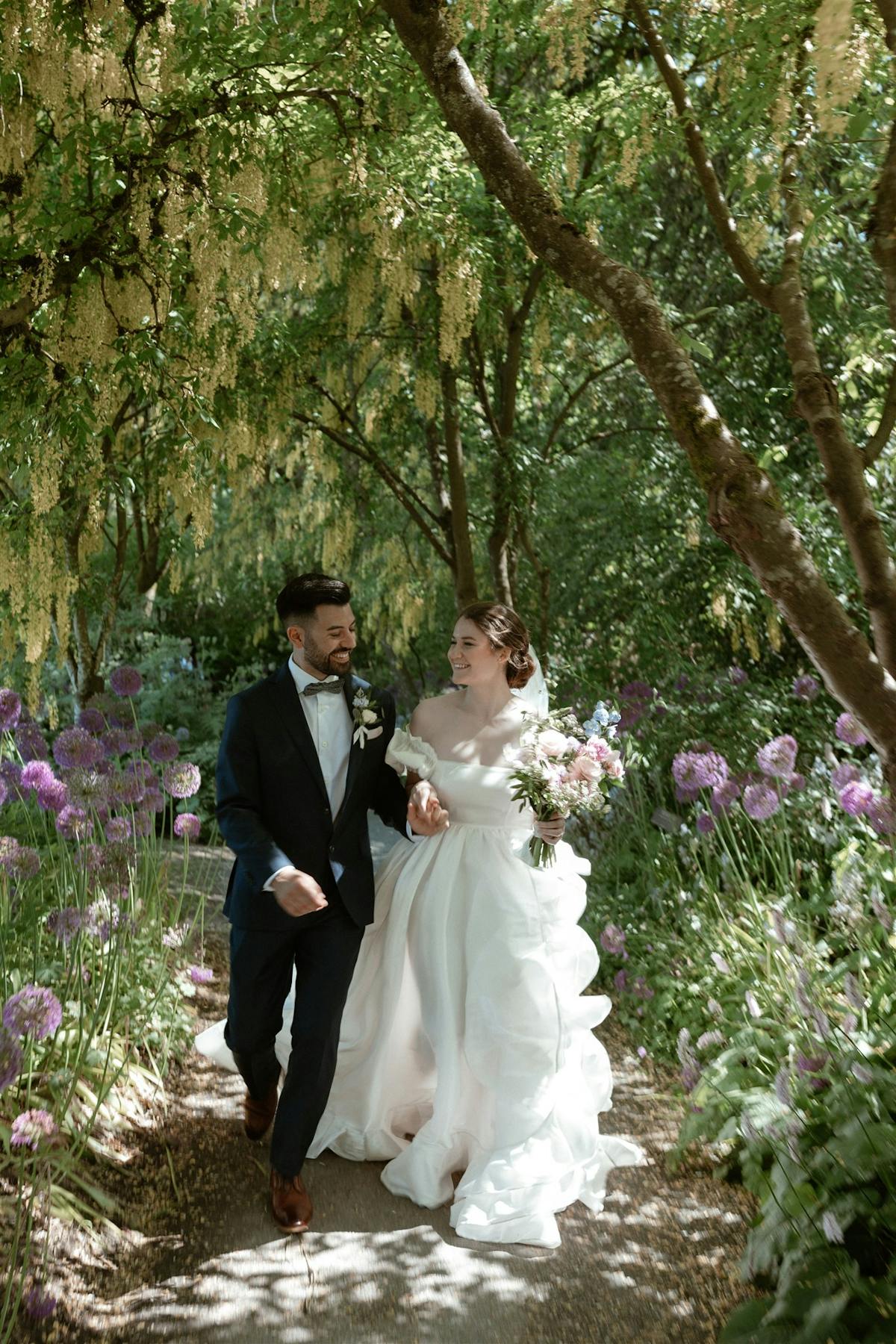 bride and groom are walking through trees at VanDusen Garden