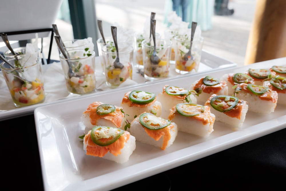 salmon sushi on platter and behind in the background with ceviche cups with spoons 