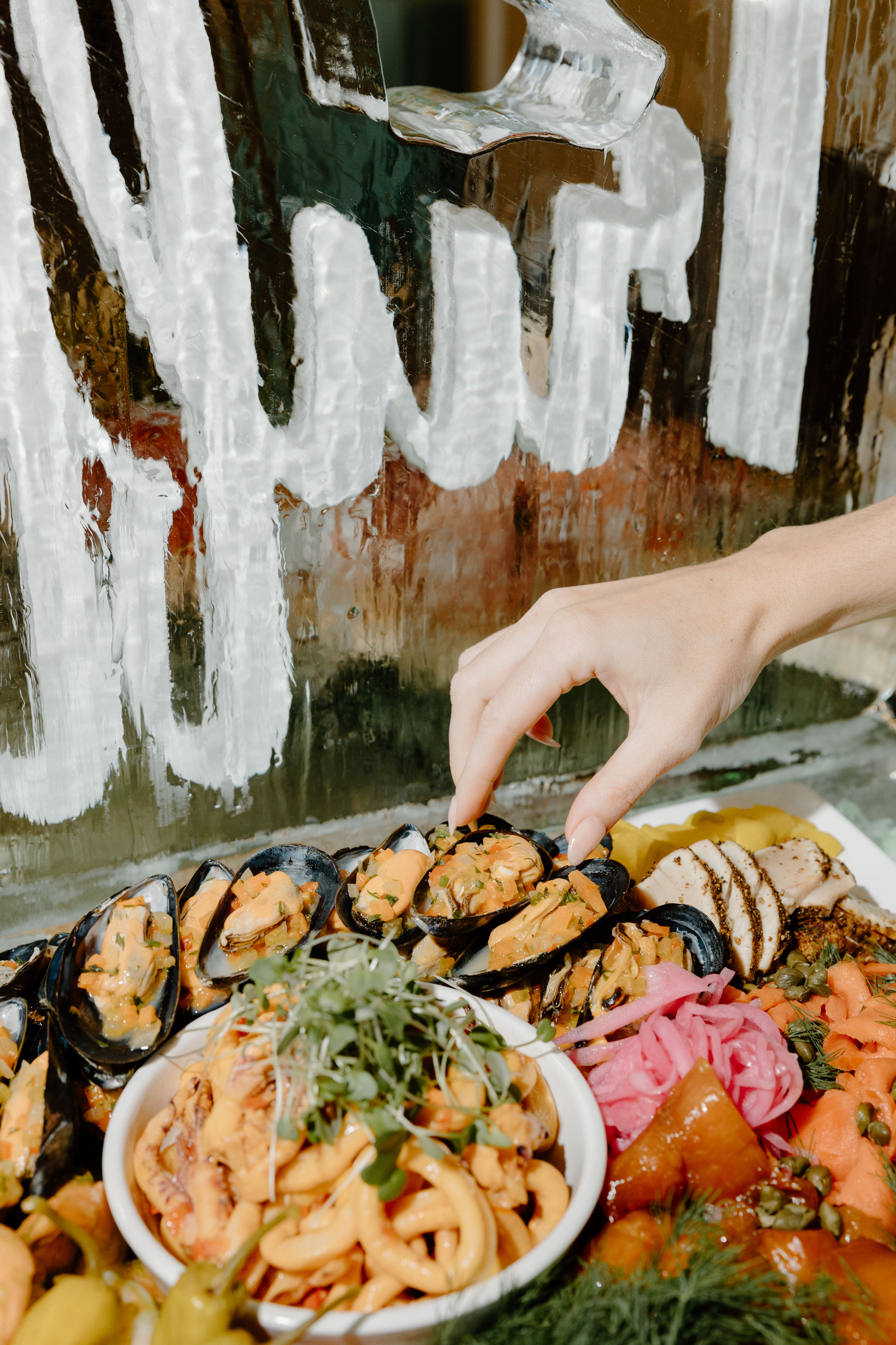 Close-up of Truffles Fine Foods' Seacuterie Platter featuring marinated mussels, pickled vegetables, smoked salmon, squid, and garnishes, with a hand reaching for a mussel at the Spring Fling 2025 event in Vancouver.