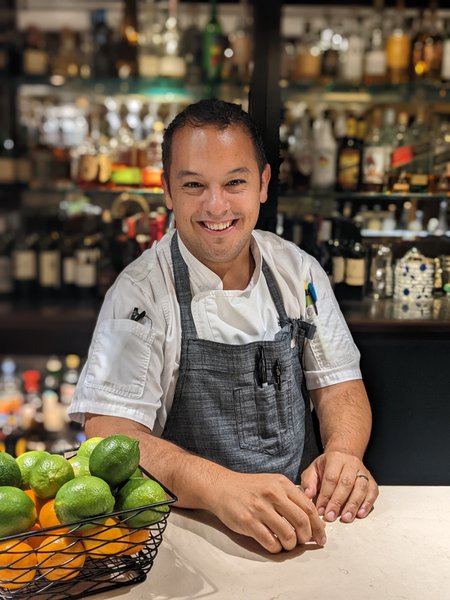 a person sitting at a table in front of a fruit stand