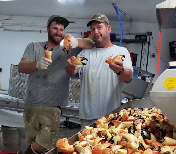 two men holding crab claws and posing for the camera