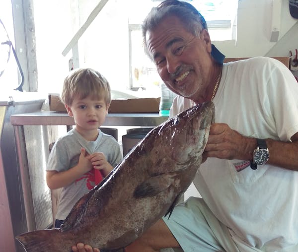 a man and a kid holding a big fish and posing for the camera