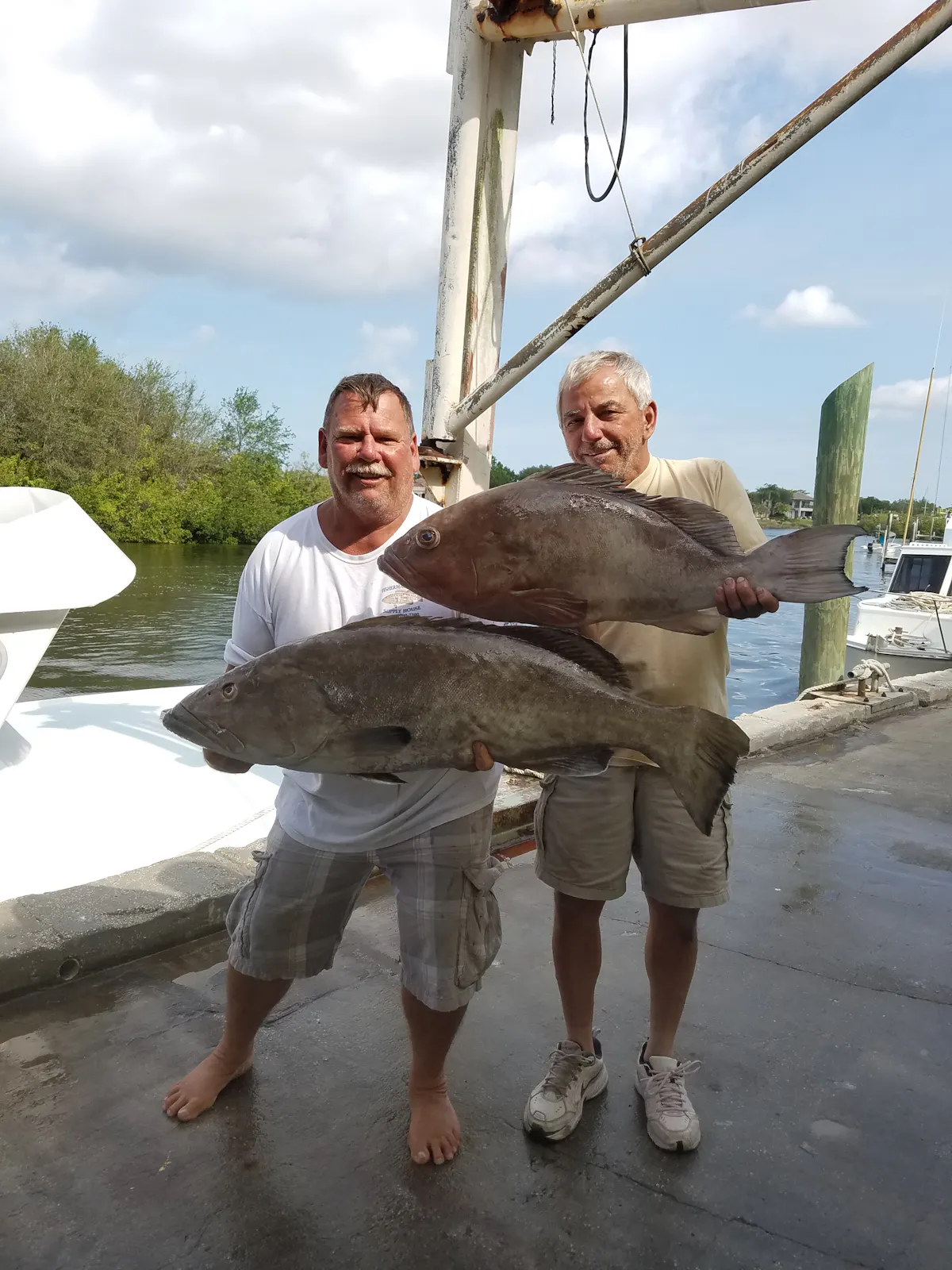two men holding a two big giant fishes