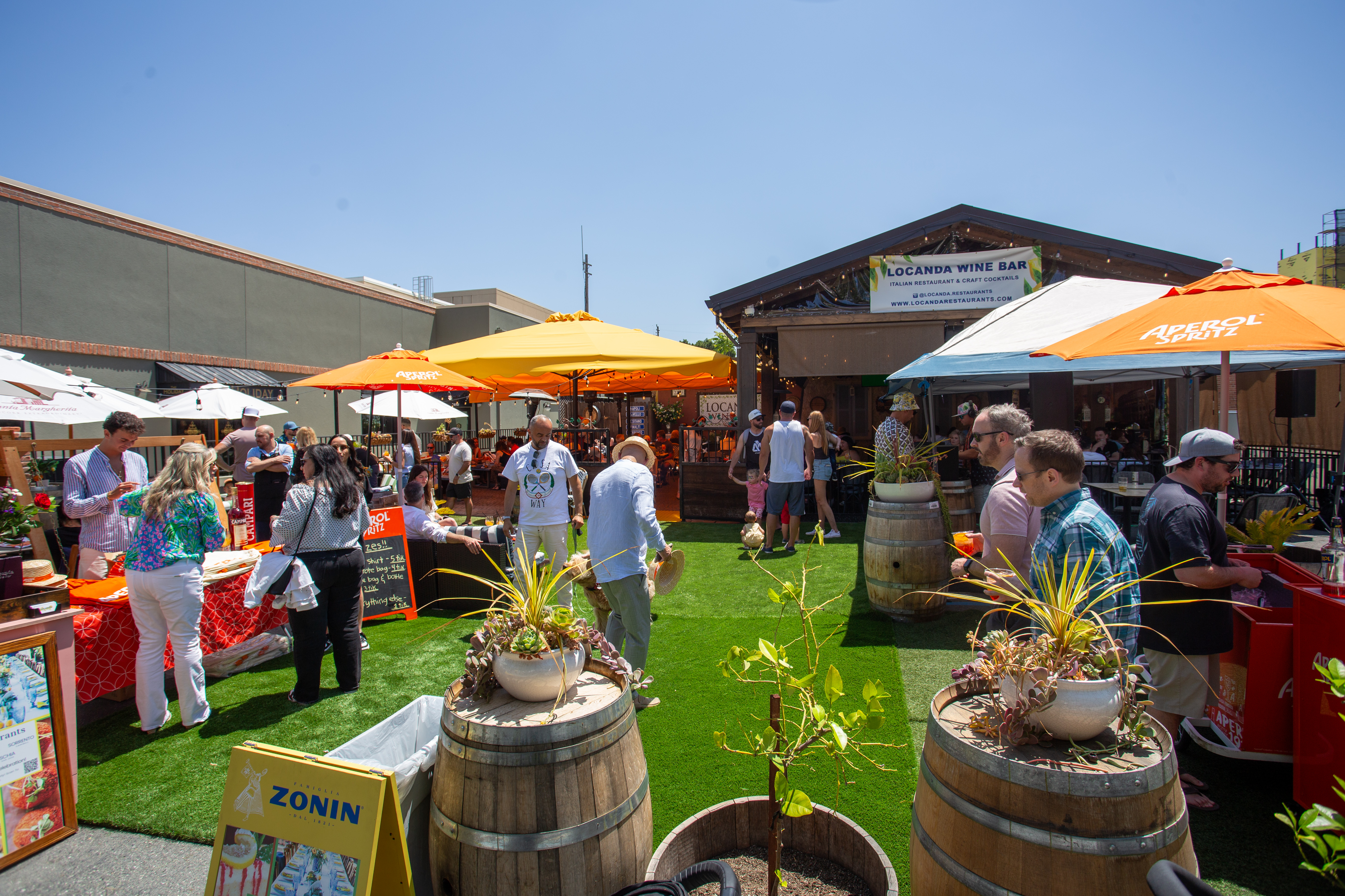 a group of people on a green lawn with umbrellas and barrels