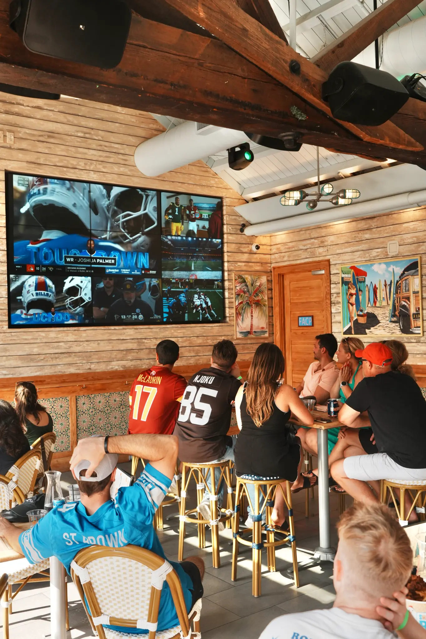 Guests watching football from tables beneath a television inside Share House