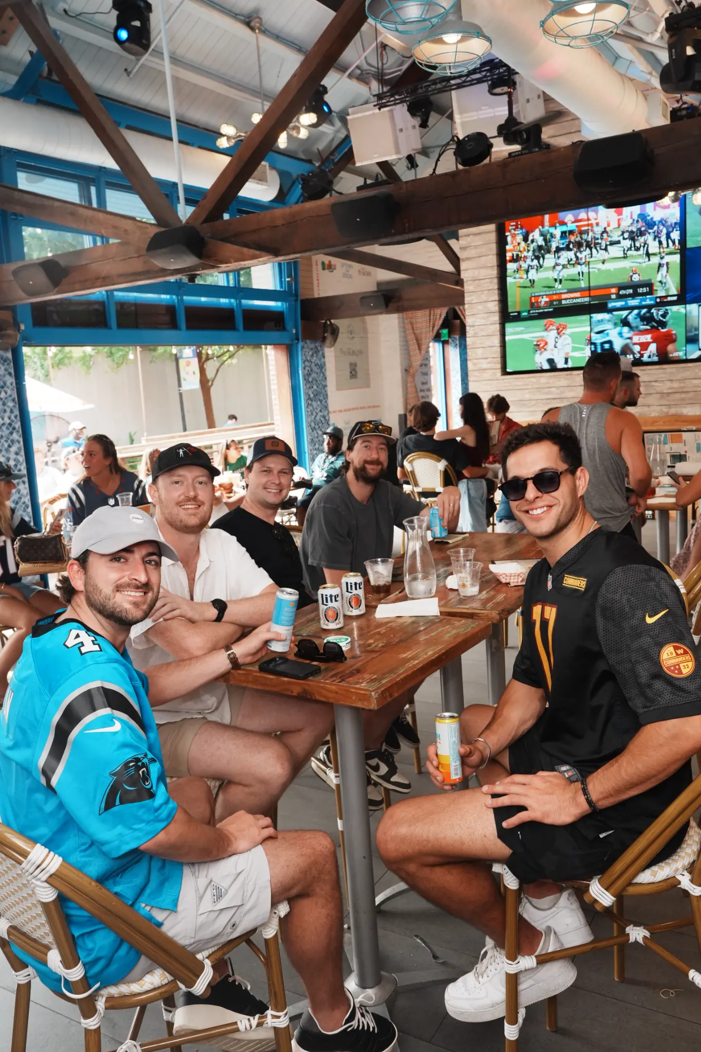 A group of football fans gathered at a table by the open blue doors of Share House