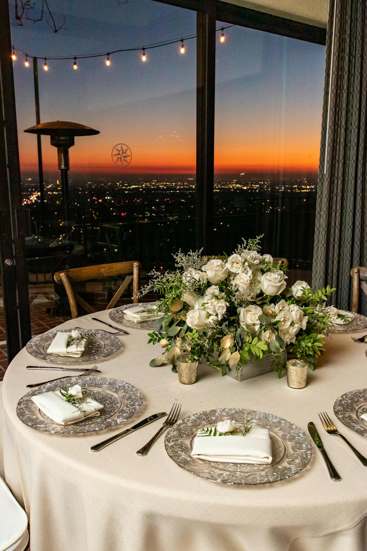 flowers sitting on top of table with sunset view large windows