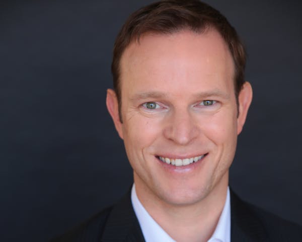 a man wearing a suit and tie smiling at the camera