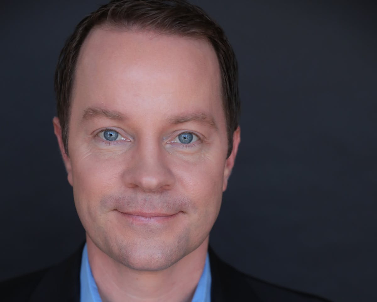 a man wearing a suit and tie smiling at the camera
