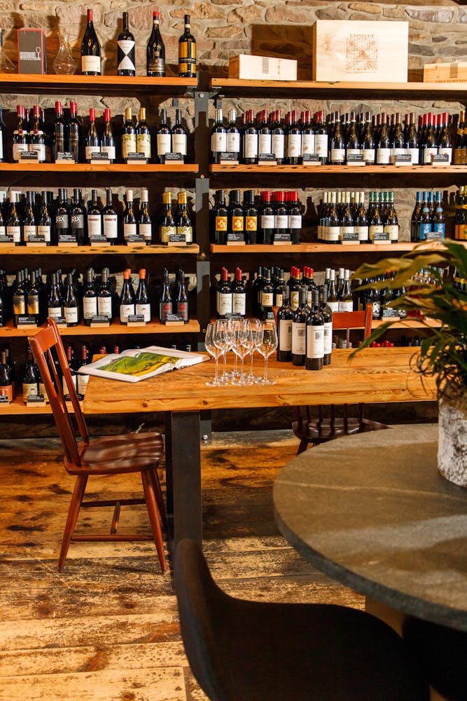 bottles of wine sitting on top of a wooden table in front of wooden shelves filled with wine bottles