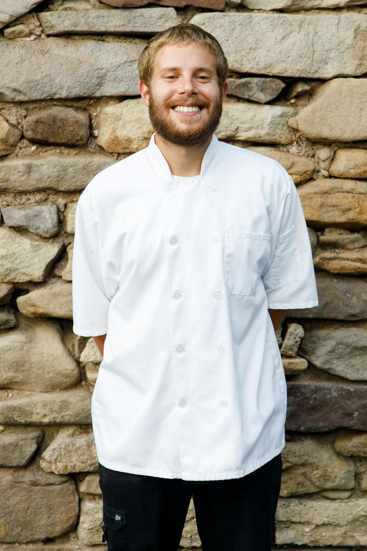 a man wearing a chef's jacket in front of a stone wall