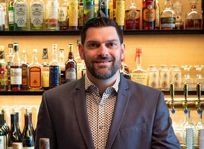 a man sitting at a table with wine glasses and smiling at the camera