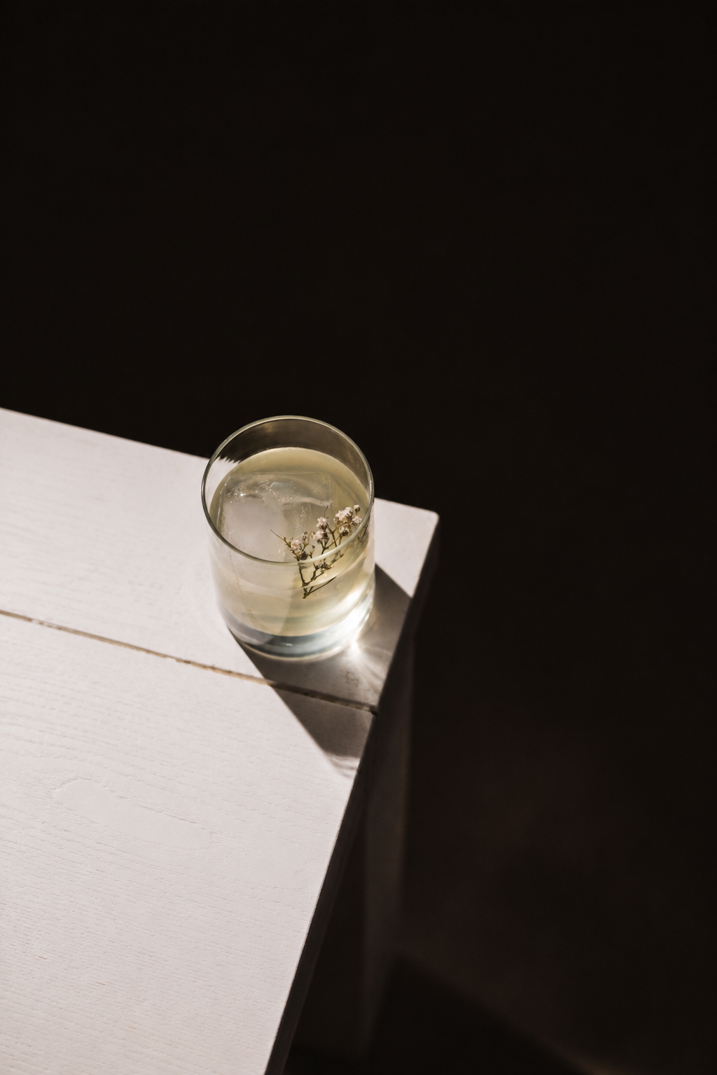 a glass of liquid with ice and flowers on a white surface