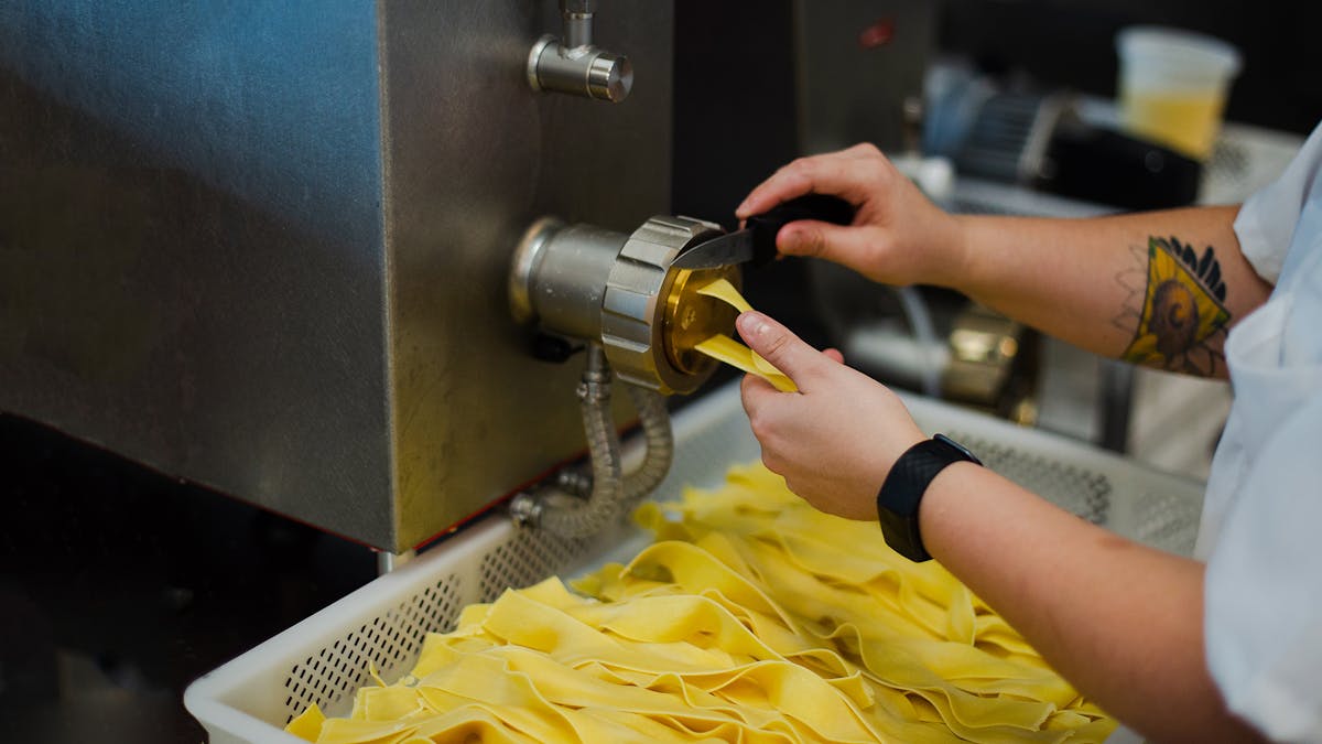 close up of hands making fresh pasta from an extruder