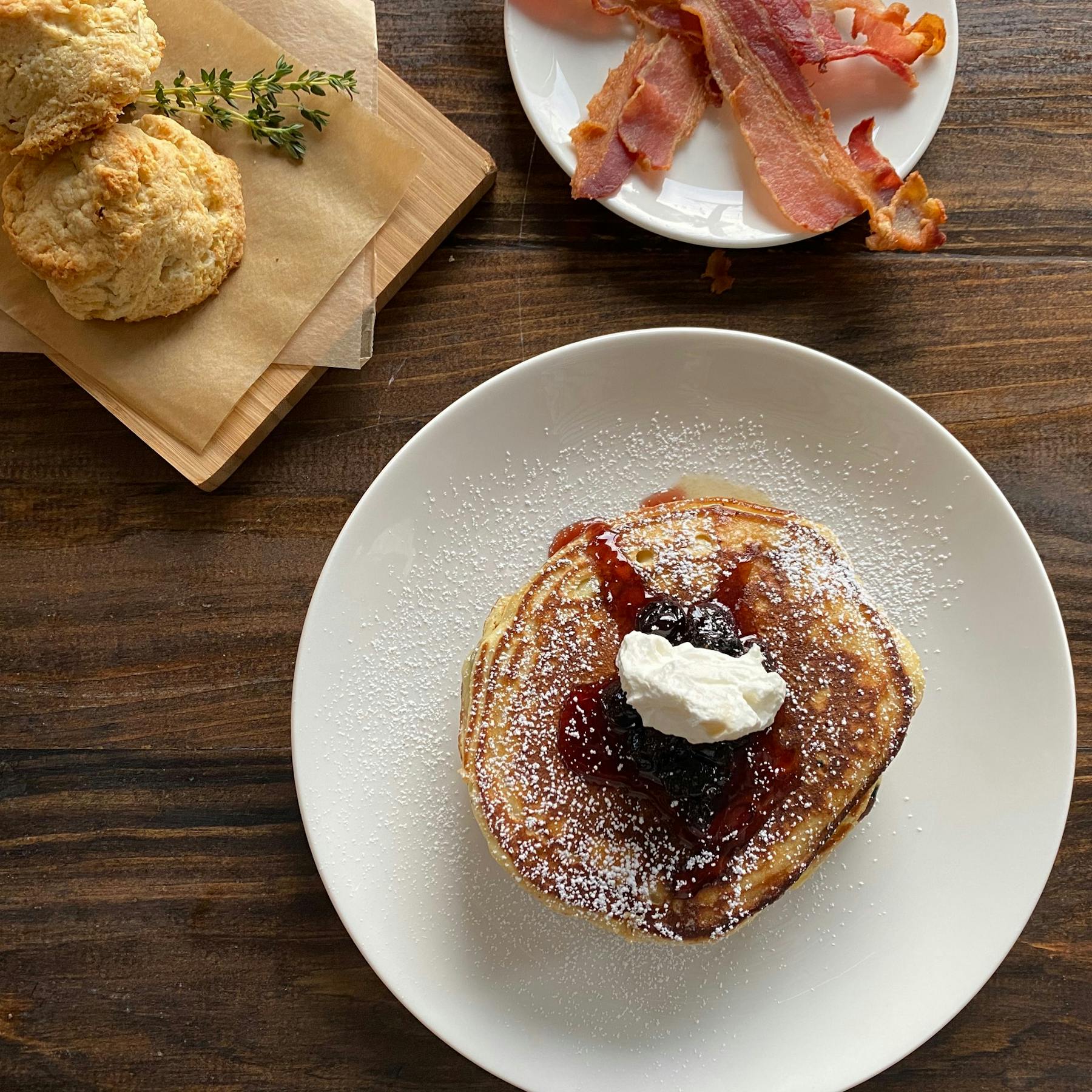 a table with pancakes, bacon, and biscuits