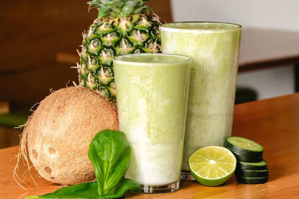 a glass of green smoothie next to a pineapple and coconut