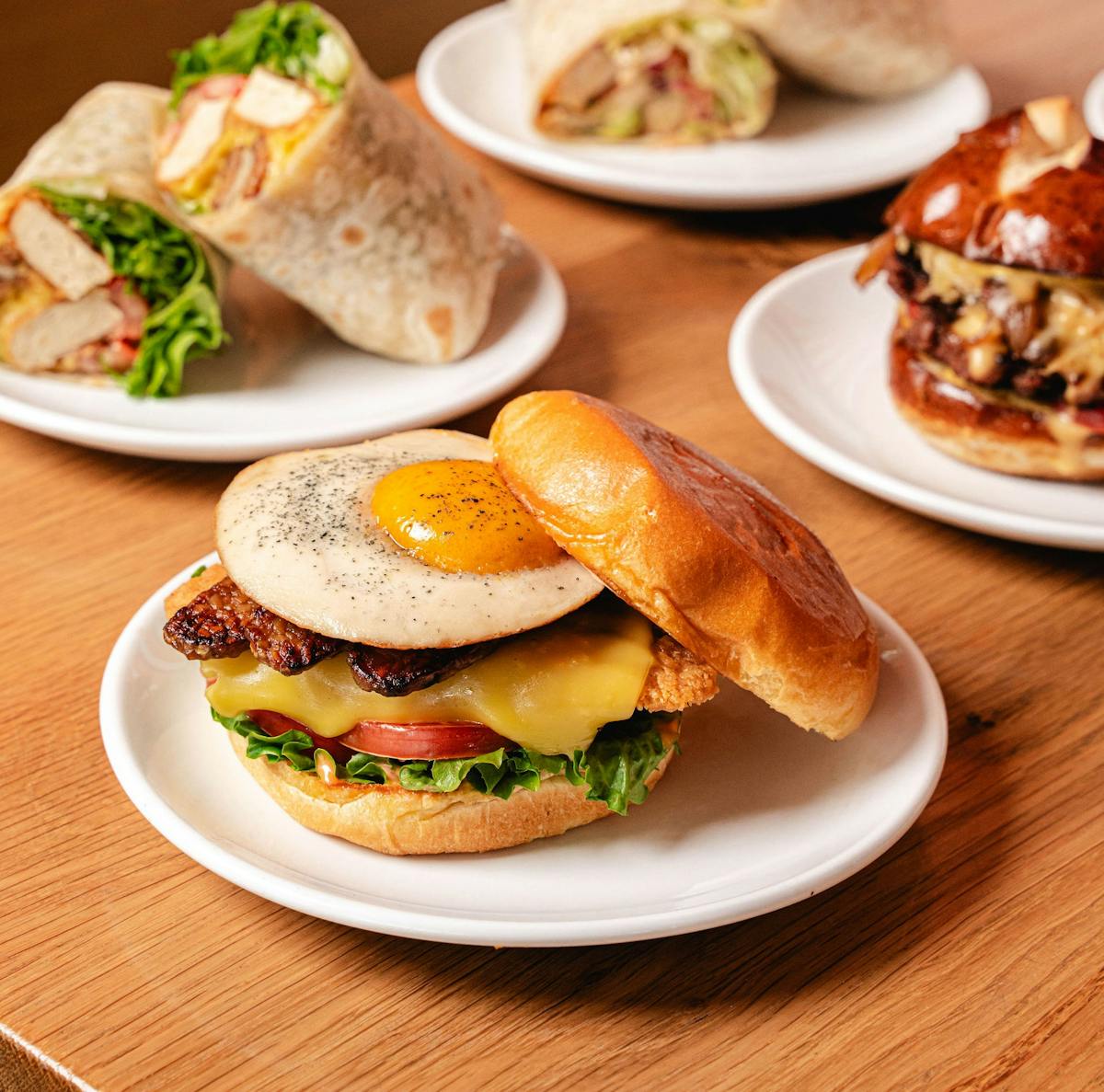 Sunrise Burger with plant-based egg and bacon, plus wraps and a cheeseburger on plates.