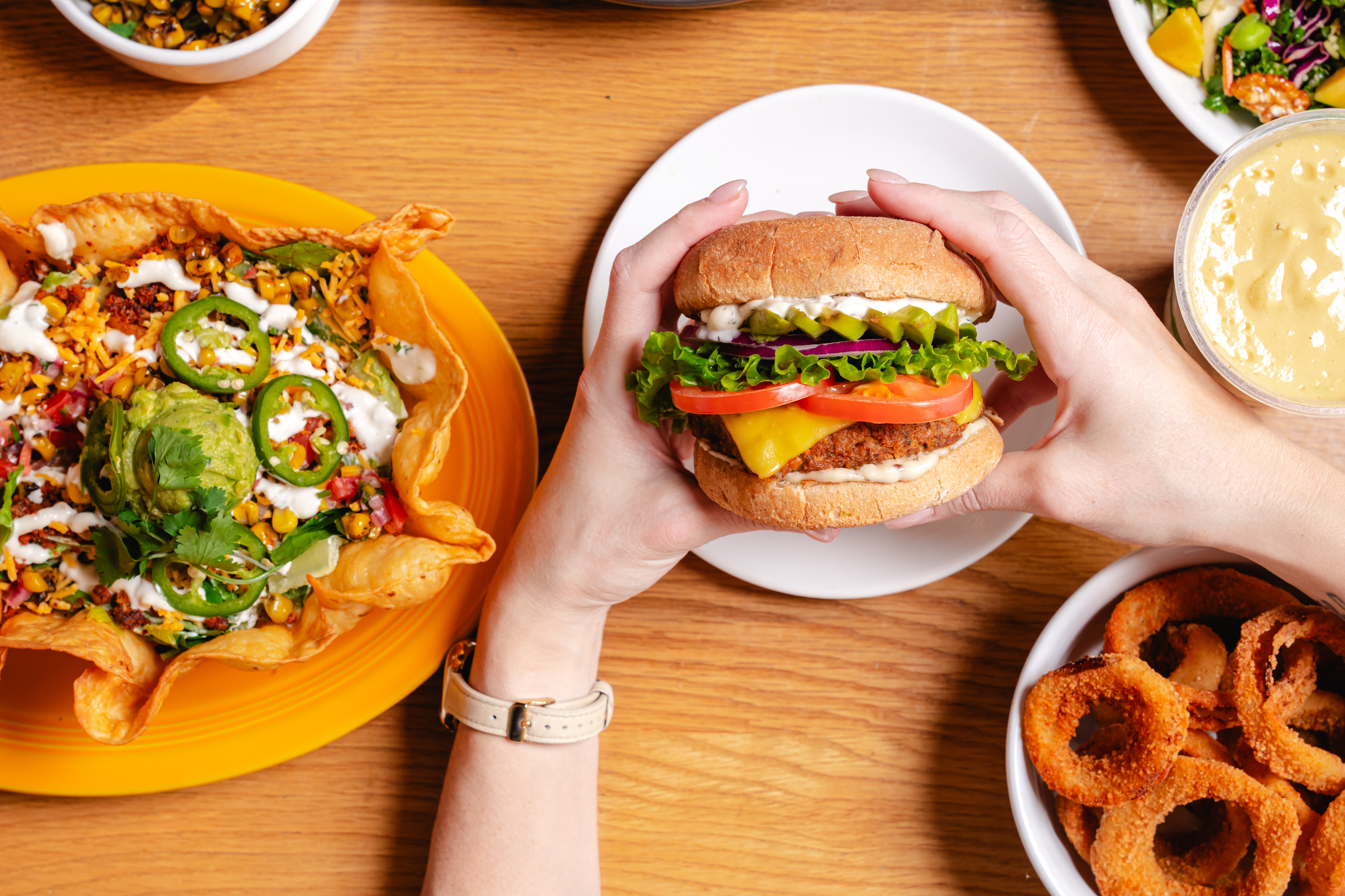a person holding a burger and a plate of food