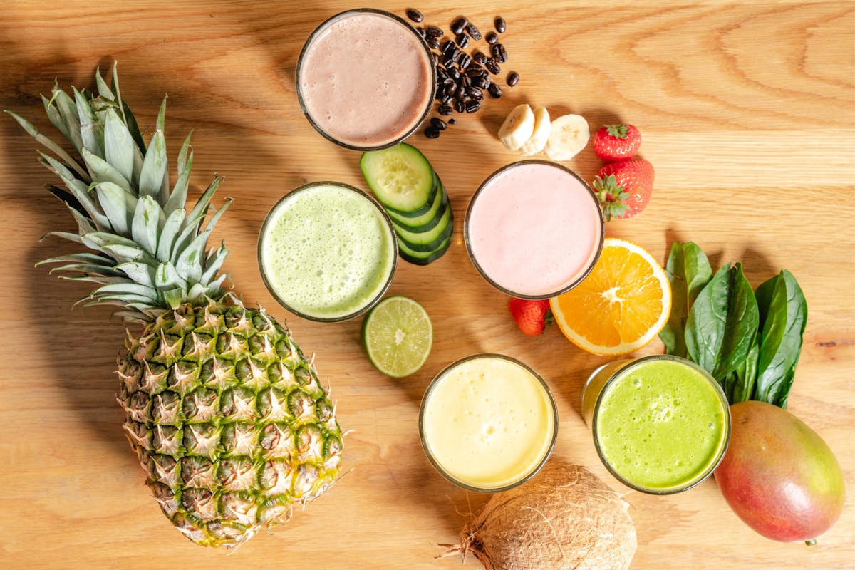 Five smoothies with fresh fruits and superfoods on a wooden table.