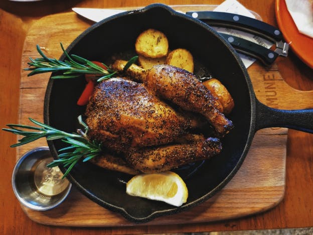 a rotisserie chicken in a pan with roasted potatoes and thyme