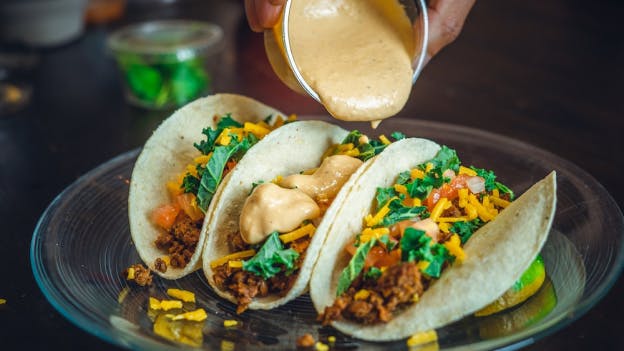 A person adding sauce to a taco on a plate