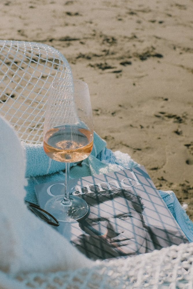 A magazine lying on the beach with a wine glass