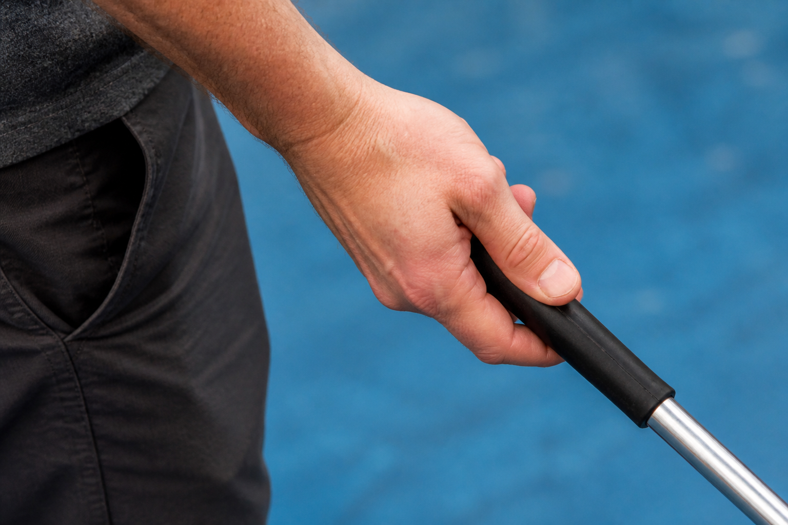 Adult hand holding the handle of a deck-shuffleboard cue