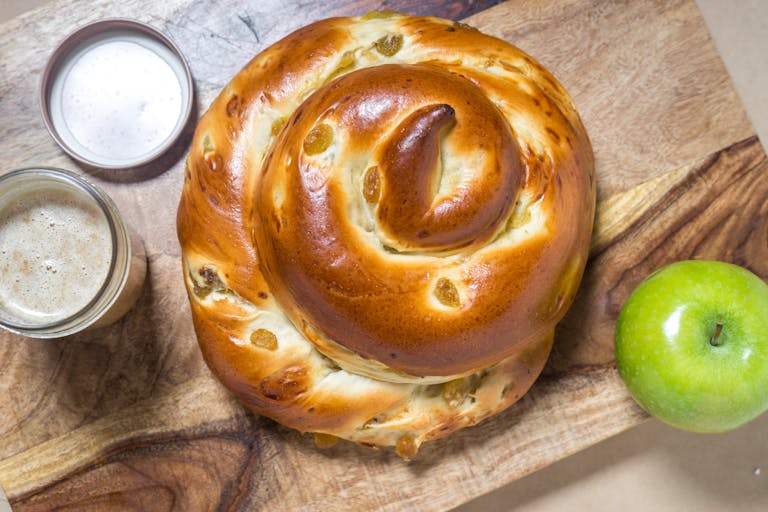 a spiral-shaped raisin challah sitting on top of a wooden cutting board