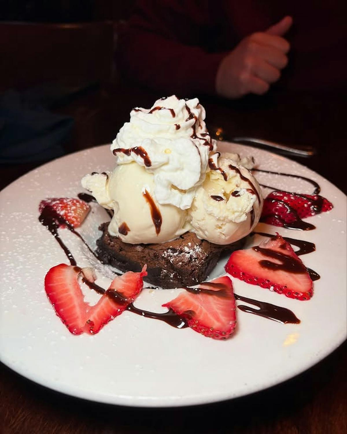 Brownie sundae on white plate with strawberries and chocolate dressing