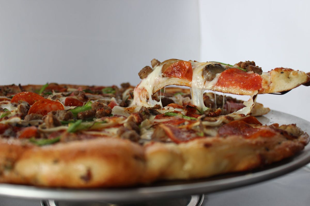 a plate of a full pizza pie with a slice of pizza being taken out