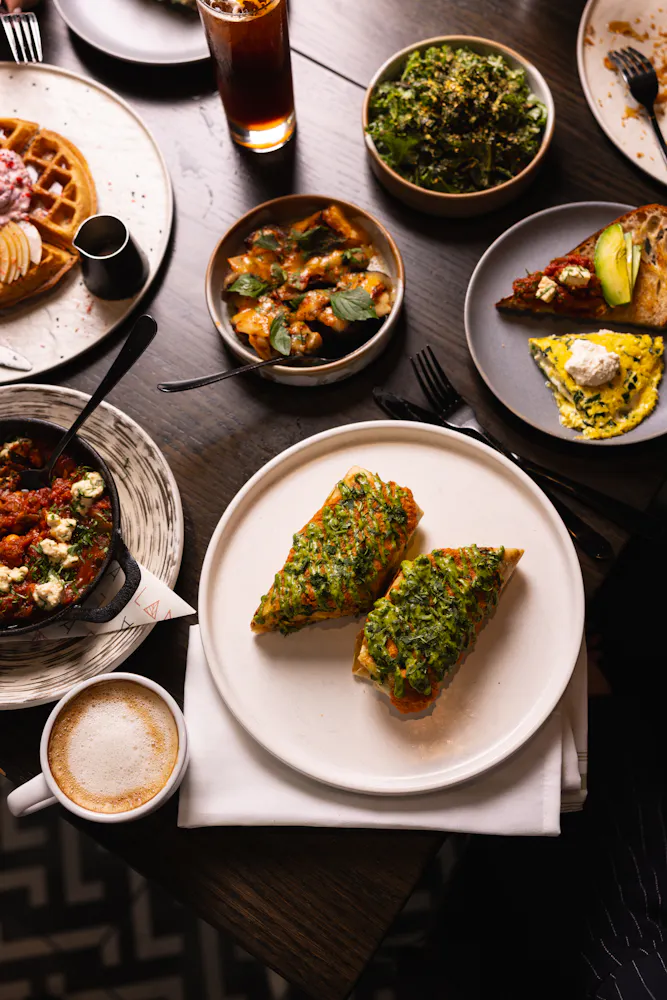Overhead view of toast topped with greens, waffles, salad, and coffee on a restaurant table.
