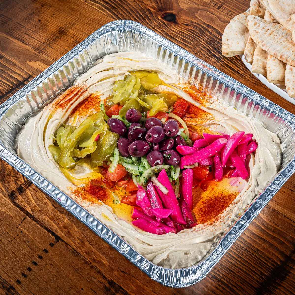 Mamoun's Hummus Tray garnished with pickles, pickled turnips, olives, paprika and olive oil, with pita on the side
