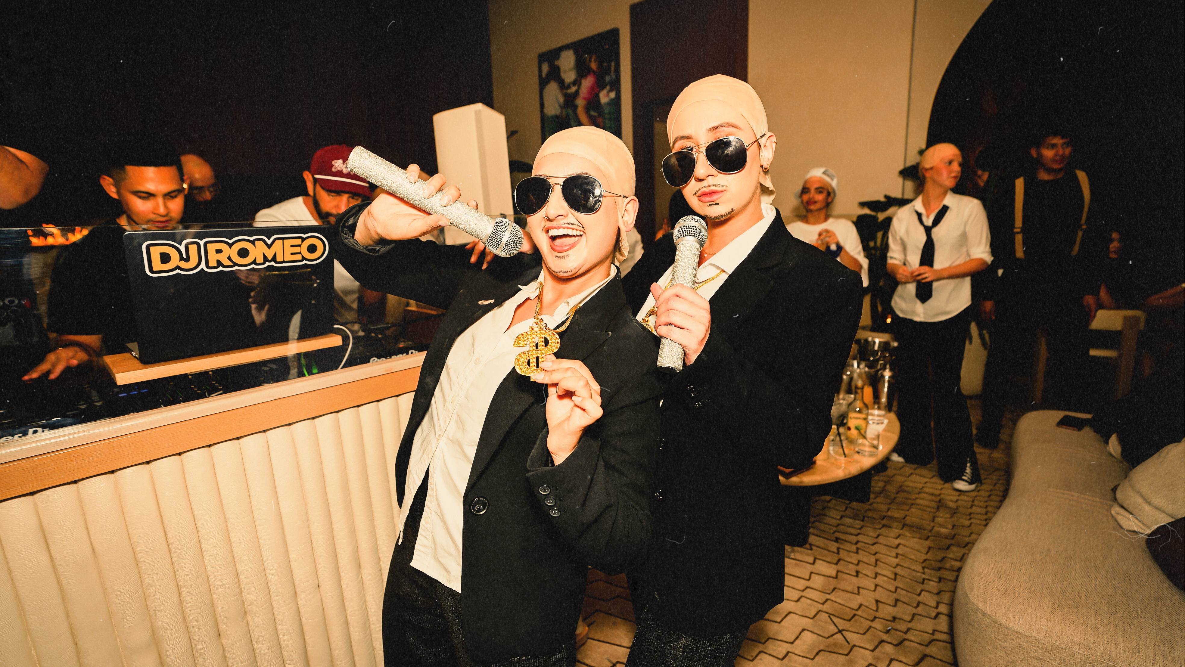 Two women dressed as Pitbull at Bel-Aire Lounge in Las Vegas pose with microphones and dollar-sign chains in front of DJ Romeo’s booth during Baldies Worldwide 2, a high-energy ladies night at the best local lounge.