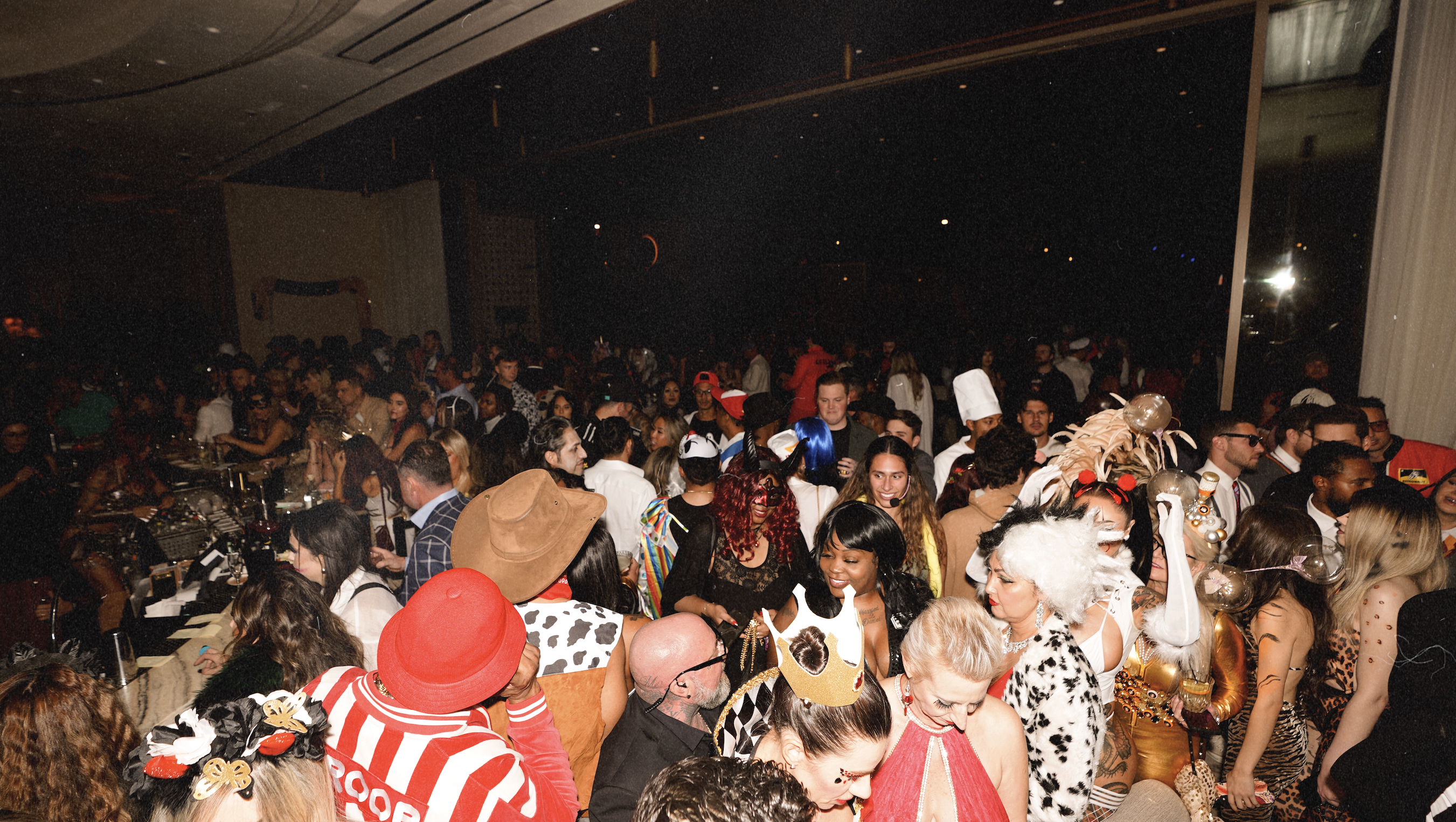 Packed dance floor at Bel-Aire Lounge during a Halloween party. Dozens of guests in costumes including cowboys, Cruella de Vil, and colorful wigs crowd the bar and mingle under dim nightlife lighting.